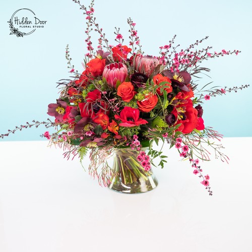 Red protea roses and hellebores with cherry blossom branches in a glass bowl from Durham flower studio