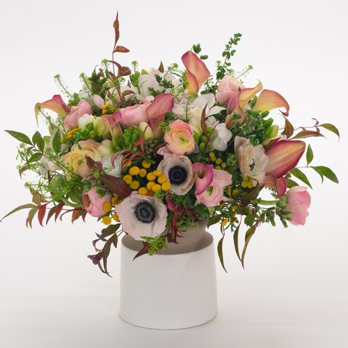 White anemones pink calla lilies ranunculus and yellow craspedia in a ceramic vessel by Durham flower delivery
